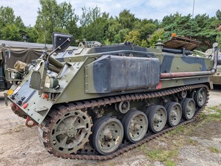 Military vehicle parked in a forested area during daytime in an outdoor display setting