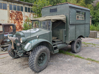 Fototapeta premium Vintage military truck parked near old industrial buildings in a rural setting