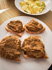 Four slices of bread with chicken liver pate and egg salad in the background