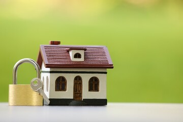 Home security. House model, key and padlock on white table outdoors, closeup. Space for text