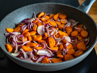 Frying carrots and red onion in frying pan on induction cooker