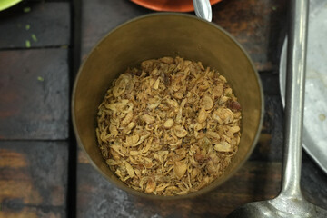 Crispy fried onions are placed in a container on a wooden table.