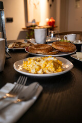 A plate of eggs and toast sits on a table in a dimly lit room. The table is set with a variety of dishes and utensils, including a fork, knife, and spoon. Scene is cozy and inviting