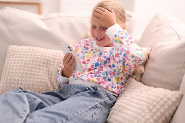Smiling little girl with smartphone on sofa at home