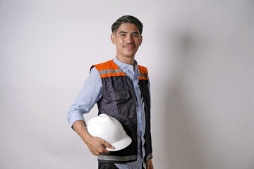 An Asian man wearing a safety vest holds a white helmet in one hand and looks at the camera with a smile. Construction workers. An architect looks at a modern building.