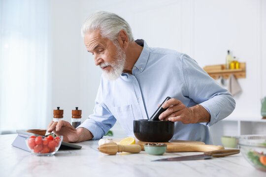 Elderly man using tablet while cooking at white marble table in kitchen