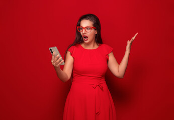 Furious woman talks to mobile phone, isolated on red background. Rage girl holding spoiled...