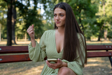 Frustrated young woman using smartphone on park bench, outdoor lifestyle, social media and technology concept