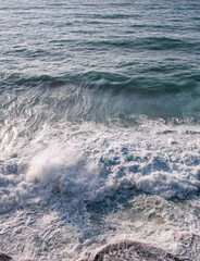 Sea water with foamy surface and waves. Close-up top view of green and blue rushing water near the shore