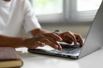 Black man's hands are pressing the keyboard on a laptop.