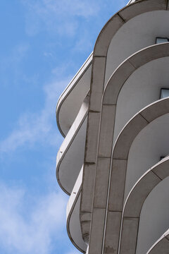 Architectural close up of flowing curved balconies in modern high rise apartment facade with geometric white surfaces under blue sky emphasizing clean lines and contemporary design