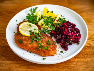 Breaded chicken breast with boiled potatoes and beets on wooden table	