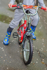 Fototapeta premium little girl riding a bike.A small cyclist pedals joyfully through a rainy path, leaving ripples in the puddles behind.