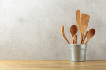 Wooden kitchen utensils in small bucket on a kitchen table.