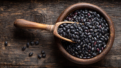 Rustic Still Life of Raw Black Beans in a Carved Wooden Bowl with a Scoop on a Dark Wood Table