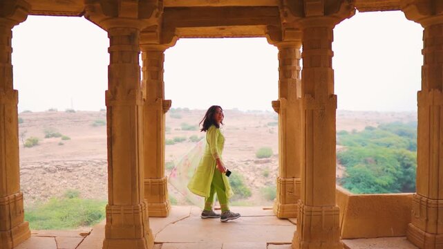 Indian woman wearing Salwar Suit and twirling while standing between architectural columns of Bada Bagh, Jaisalmer, India. Travel and holidays concept. Indian woman travel. 