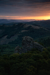 A landscape of the Sauerland region in Germany, with the Bruchhausen Steine ​​rocks in the foreground. In the background, hills illuminated by the rising sun. Vertical view