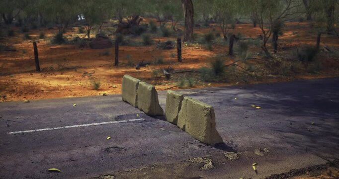 A row of rugged stone blocks sits on a dusty road, surrounded by arid terrain and scattered shrubs.