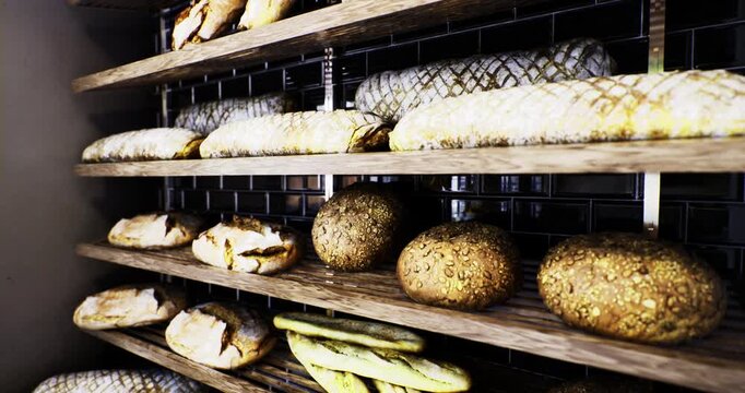 Various types of freshly baked artisan bread rest on wooden shelves inside a warm and inviting bakery. The artisanal loaves showcase a crusty exterior and are perfectly arranged.