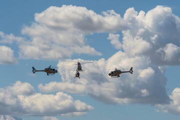 Three helicopters flying in formation against a cloudy blue sky.