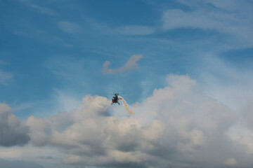 Helicopter flying solo with smoke trail over dramatic clouds.