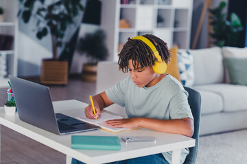 Teen boy studying with headphones while focused on a laptop in a cozy modern living room