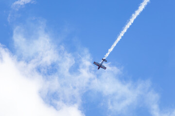An aerobatic plane performs an aerobatic maneuver in the cloudy sky with smoke trail