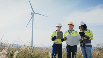 View from below of group of multi-ethnic people standing together in middle of large field. Holding tablet devices and large piece of paper. Observing physical map. Expanding company business.