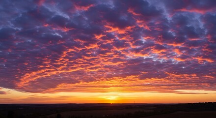 Vibrant sunset with dramatic orange and purple altocumulus clouds over a silhouetted rural landscape