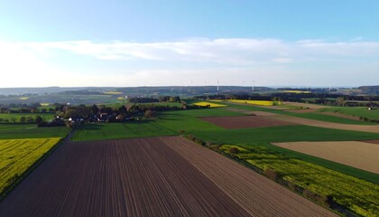 Aerial view of a patchwork of farmlands, showing fields of various colors and textures under a bright sky
