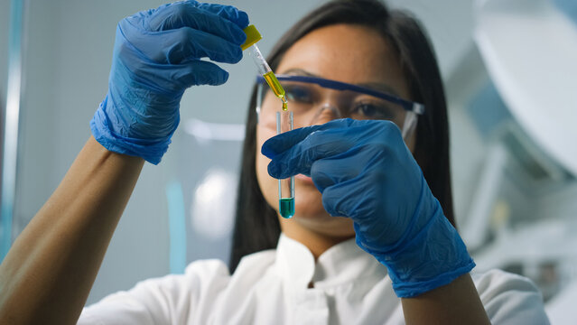 Woman scientist in protective gear measures liquid into a test tube while focused on the research task in the lab.