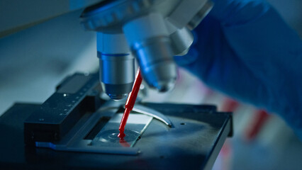 A researcher examines a blood sample under a microscope in a laboratory setting, focusing on detailed observation.