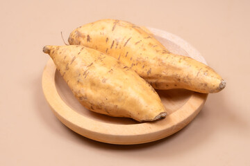 Two Cilembu sweet potatoes placed on a wooden plate with plain background, highlighting their natural texture and appeal as a healthy organic tropical food ingredient.