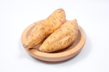 Two fresh Cilembu sweet potatoes placed on a wooden plate with clean white background, highlighting natural texture, earthy color, and rustic appeal for healthy food concepts.