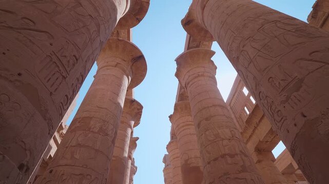 low angle shot capturing the grandeur of the ancient Karnak Temple complex in Luxor, Egypt. The footage highlights the massive, intricately carved columns of the Great Hypostyle Hall, adorned with det