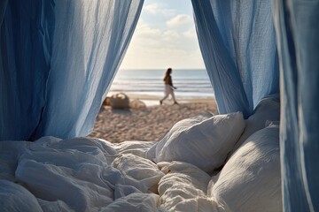 Beachfront bed with blue draped canopy. Soft white linens and a blurry figure walking on the sand