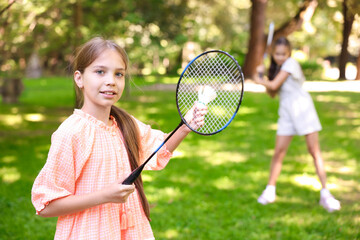 Smiling little girl with badminton racket and shuttlecock playing with her friend in park, selective focus