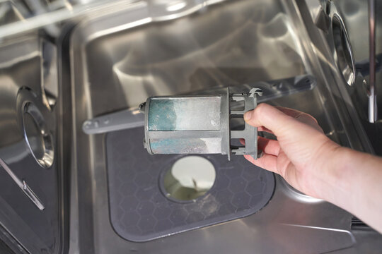 Hand holding dirty dishwasher filter over open dishwasher.