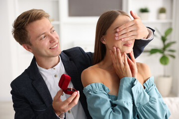 Making marriage proposal. Smiling man with engagement ring surprising his girlfriend at home