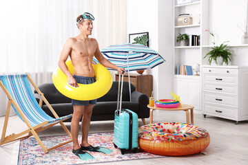 Obraz premium Happy man in flippers with diving mask, suitcase and inflatable ring at home. Dreaming about vacation at sea