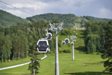 Blurred mountain cable car ride over lush green valley with dense forests and rolling hills in summer.