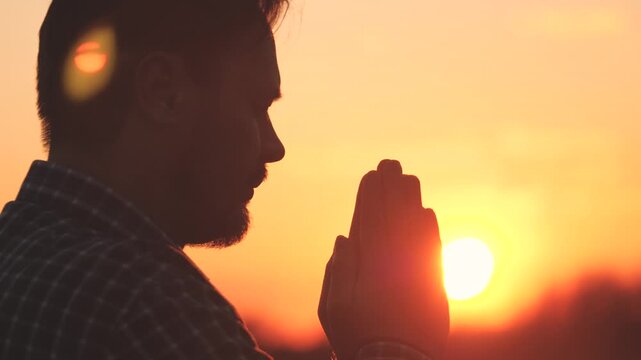 Man praying, man folded her hands in prayer silhouette at sunset. slow motion video lifestyle, man folded her hands in prayer pray to god, asks forgiveness for sins of repentance, believing man.
