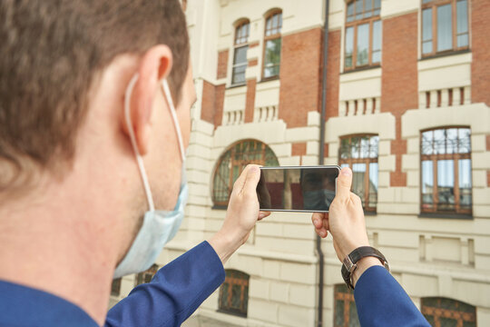 Caucasian young adult male taking photo of historic building with smartphone in urban environment.