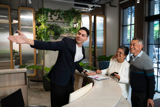 Friendly concierge assisting senior couple at modern hotel reception desk, providing direction with warm service and welcoming hospitality in a stylish urban environment.