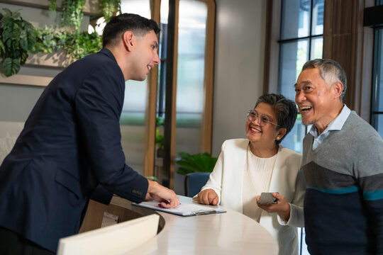 Friendly concierge assisting senior couple at modern hotel reception desk, providing direction with warm service and welcoming hospitality in a stylish urban environment.