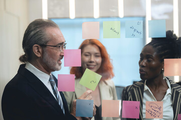 Diverse business team brainstorming ideas using sticky notes and digital tablet in modern office, teamwork and collaboration in creative planning session.