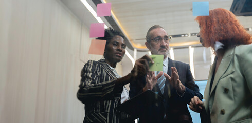 Diverse business team brainstorming ideas using sticky notes and digital tablet in modern office, teamwork and collaboration in creative planning session.