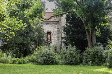 Fototapeta premium Historic stone building with a religious statue niche surrounded by dense green trees and bushes