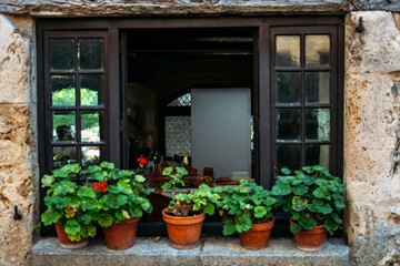 Rustic stone window with black wooden frames and terracotta flower pots filled with blooming geraniums. Rural French aesthetic, cottage renaissance, romantic facades, poetic living