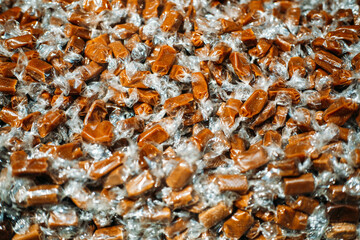 Large pile of individually wrapped caramel candies in clear cellophane wrappers under warm lighting. Nostalgic treats, handmade confections, sweet indulgence, artisanal candy culture